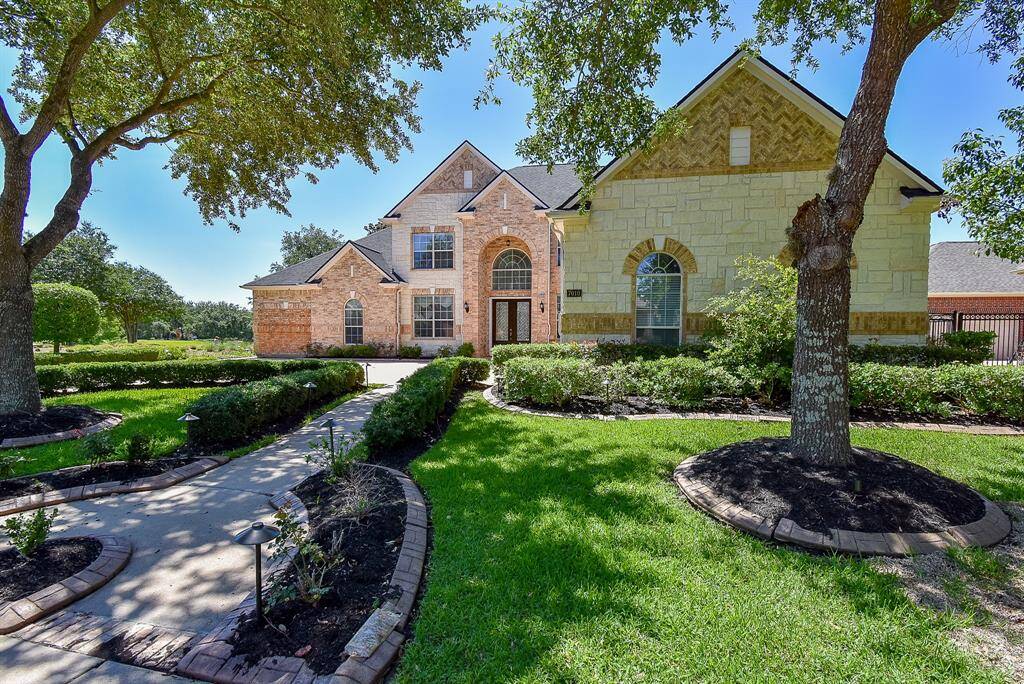 A stately façade welcomes you home, fronted by a sprawling manicured lawn, mature trees, and tidy plant beds. A long pathway leads to the grand double front doors beneath a towering arched entry.