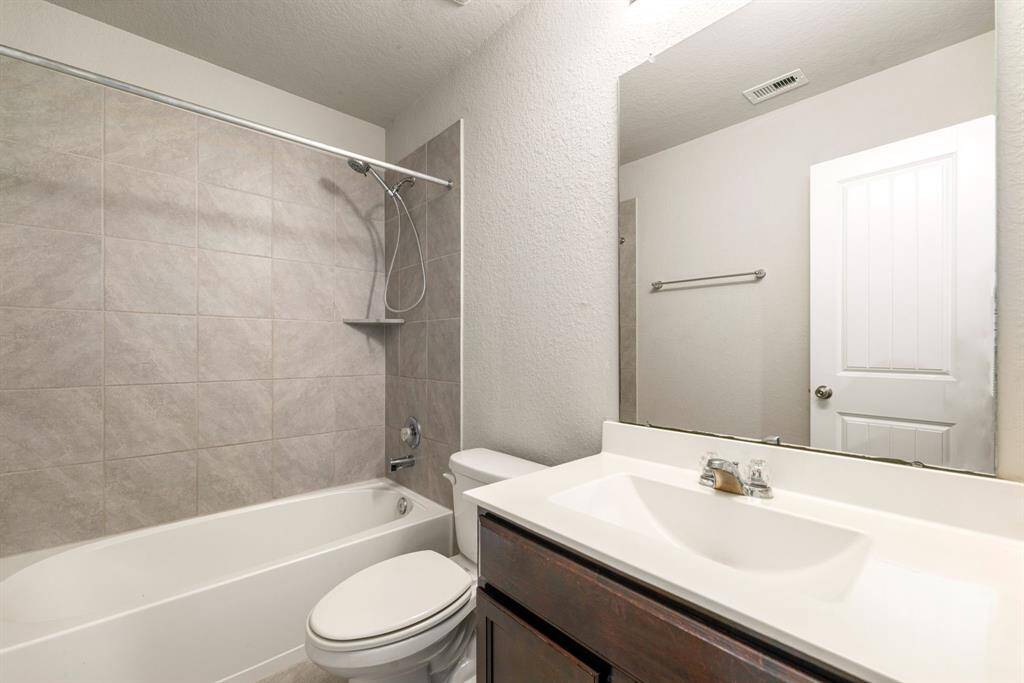 Secondary bathroom features light countertops and dark cabinets, neutral paint, shower/tub combo with tile surround, large mirror, tile floors, sleek fixtures and plenty of space to accommodate any visiting family or guests.