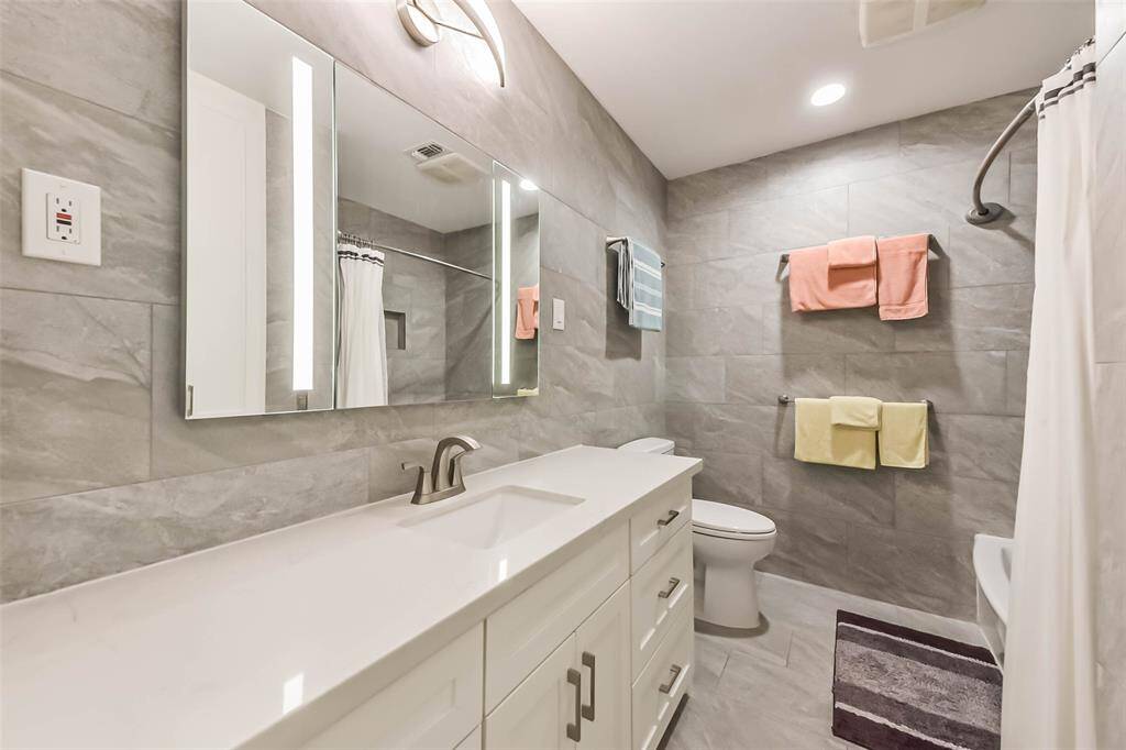 Porcelain tiles adorn walls and floor of the fully remodeled secondary bathroom  Modern light fixtures and illuminated mirrors add to the sleek and modern appearance.