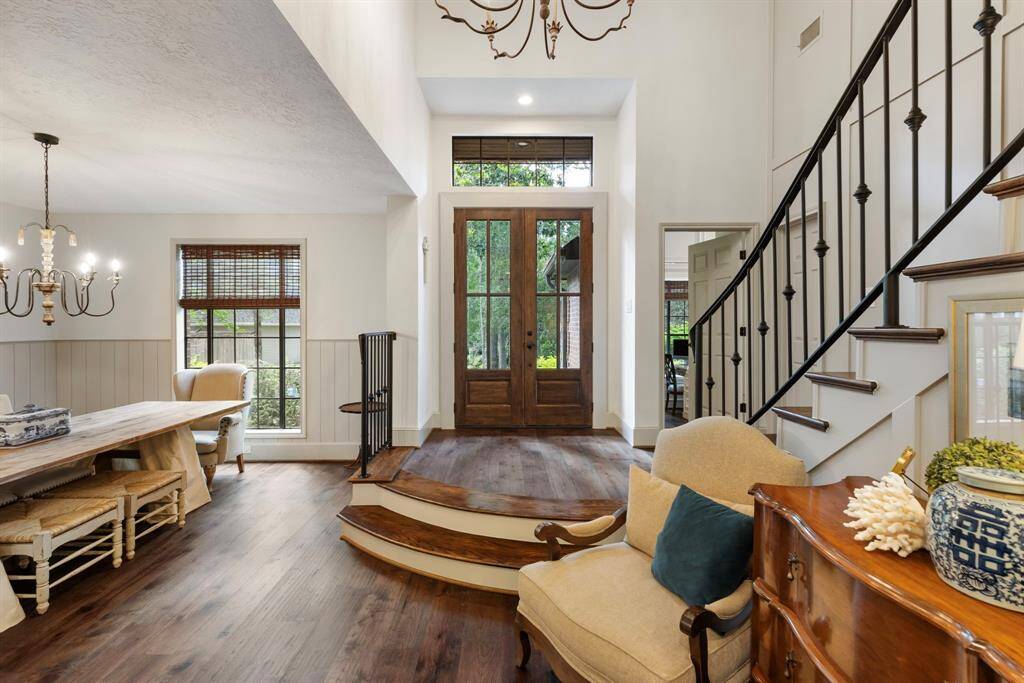 This inviting entryway features a grand wooden front door and a charming staircase with wrought iron railings. This gorgeous space is enhanced by natural light, hardwood floors, and elegant decor, including a chandelier in the adjacent dining area.