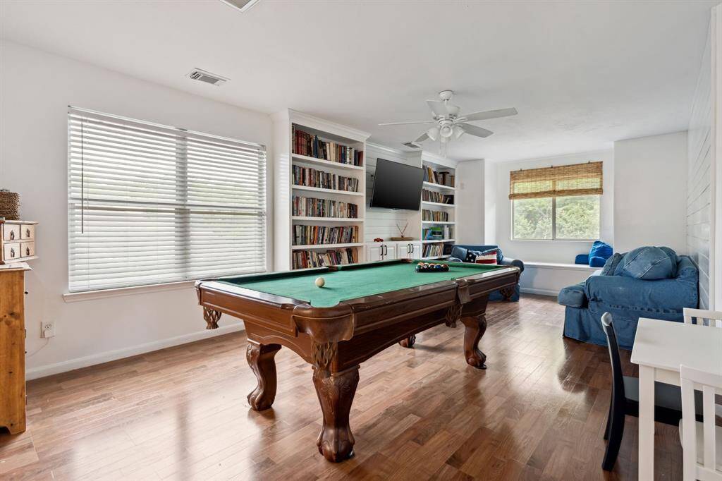 The upstairs game room features beautiful floors, large windows, built-in shelving, and a ceiling fan.