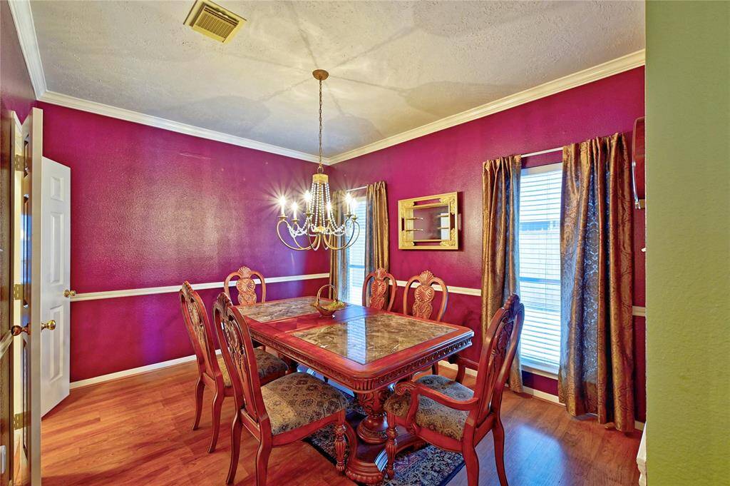 This dining room features vibrant red walls, elegant crown molding, and a classic chandelier. A large window with drapes and easy access to kitchen.