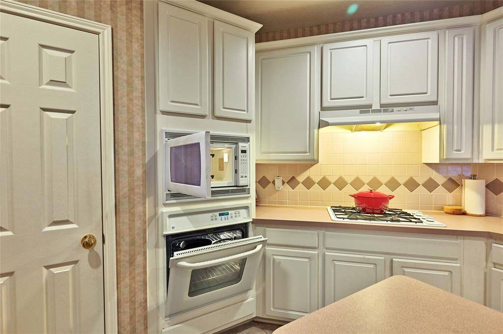 This kitchen features white cabinetry with ample storage, a built-in microwave and oven, and a gas stovetop. The light-colored countertops and tiled backsplash add a warm touch.