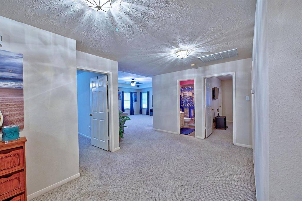 This photo showcases a spacious and well-lit second floor hallway with textured ceilings and carpeted flooring. It features multiple doorways leading to other rooms.