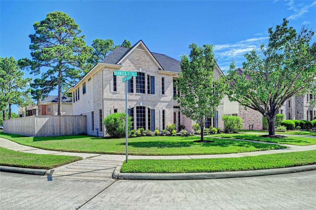This photo shows a beautiful two-story brick house on a corner lot with well-maintained landscaping and mature trees. It features a spacious front yard with a sidewalks.