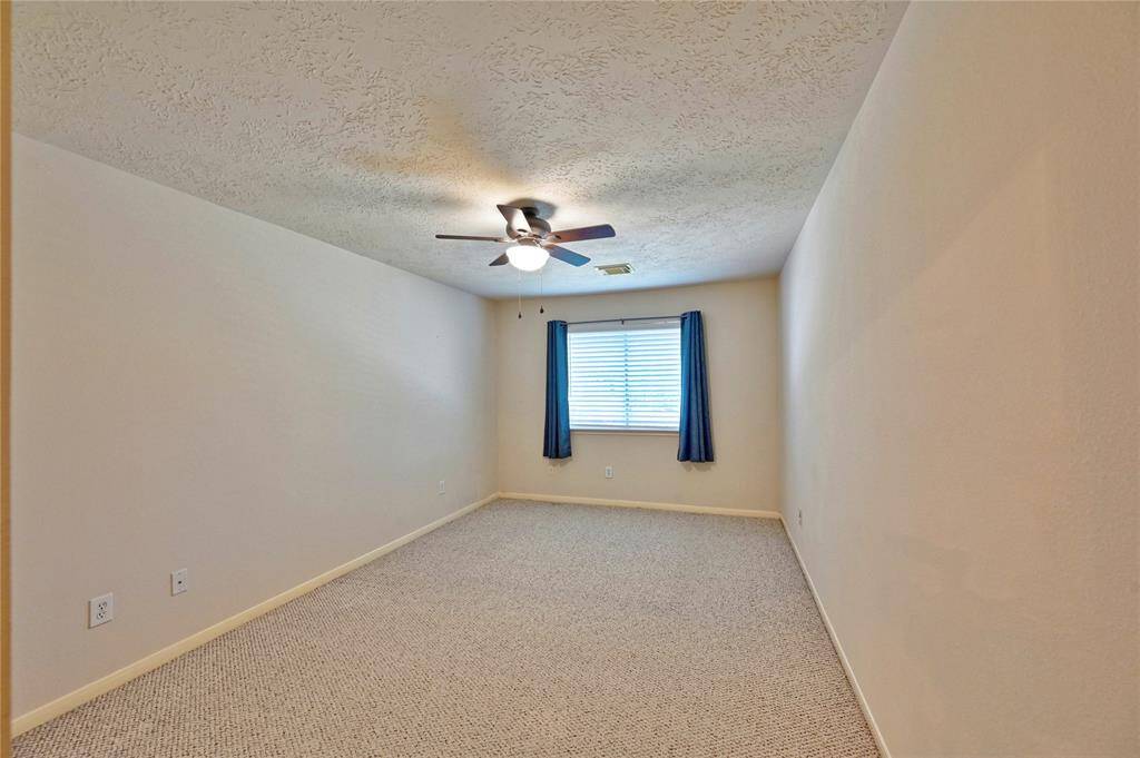 Bedroom 3 features neutral walls, carpeted flooring, a ceiling fan with light, and a window with blue curtains, and walk in closet.