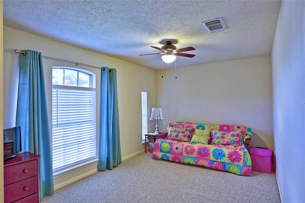 Bedroom 4 featuring a bright, large window with blue curtains, ceiling fan, and neutral walls, and walk in closet.
