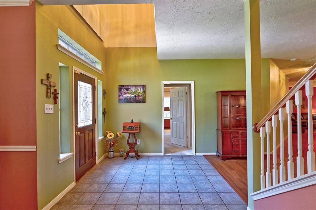 This welcoming entryway features a stylish front door with decorative glass, tile flooring, and a staircase with wooden accents. The space is enhanced by warm, colorful walls and a bright, inviting atmosphere.