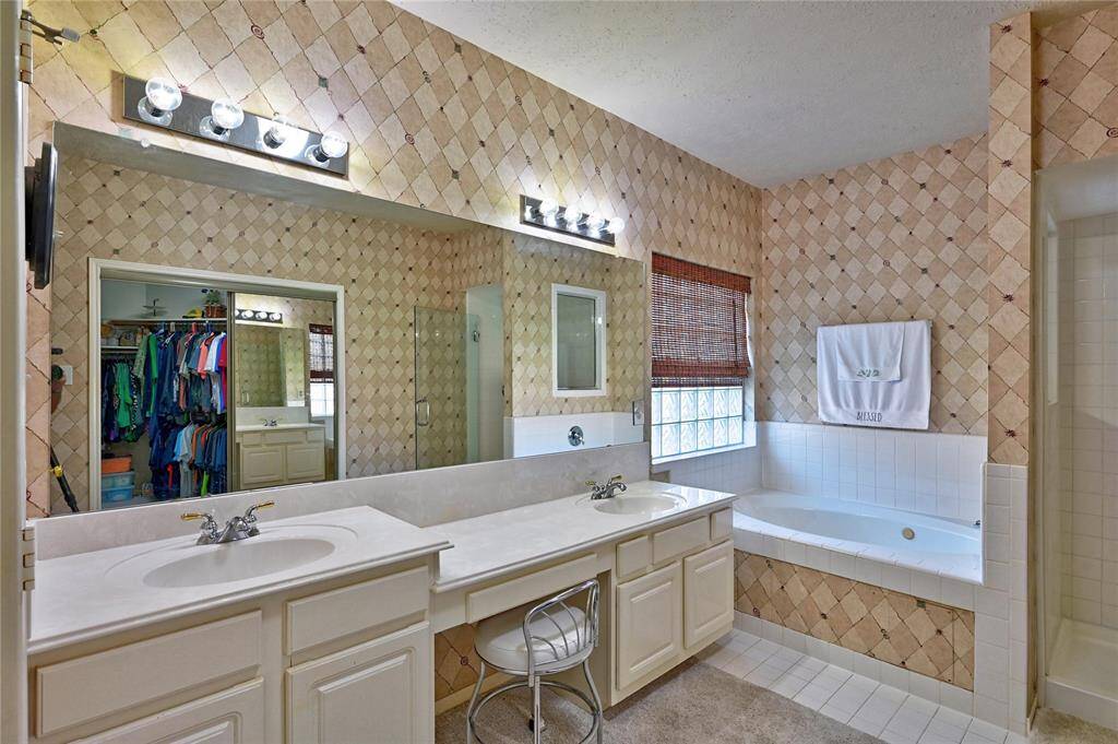 Spacious bathroom with dual sinks, a large vanity, and a relaxing corner bathtub. Features a separate shower, ample lighting, and a walk-in closet for convenient storage.