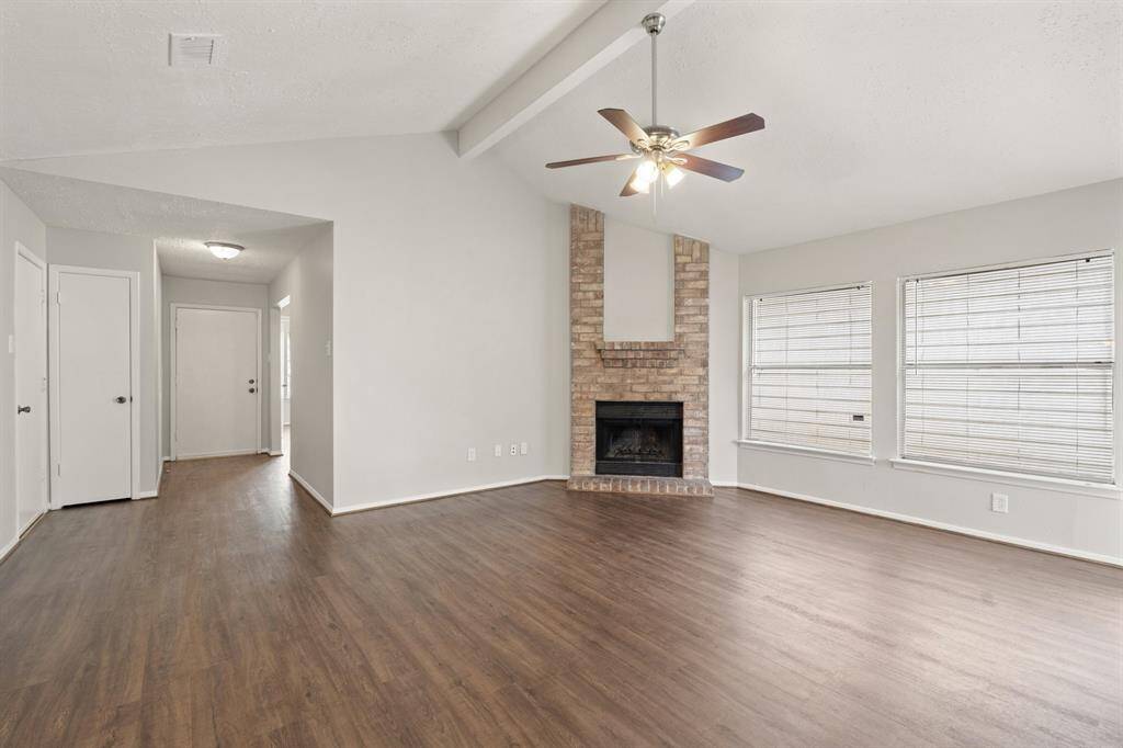 The exposed beam and high ceilings elevate the space with architectural charm, while the floor-to-ceiling corner brick fireplace stands as a stunning focal point, adding warmth, character, and a cozy ambiance to the living area.