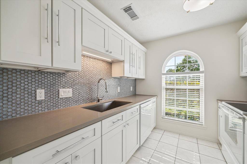 Upgraded kitchen with quartz countertops, mosaic tile backsplash, deep basin sink, and white shaker cabinets. Bright space with natural light from arched window.