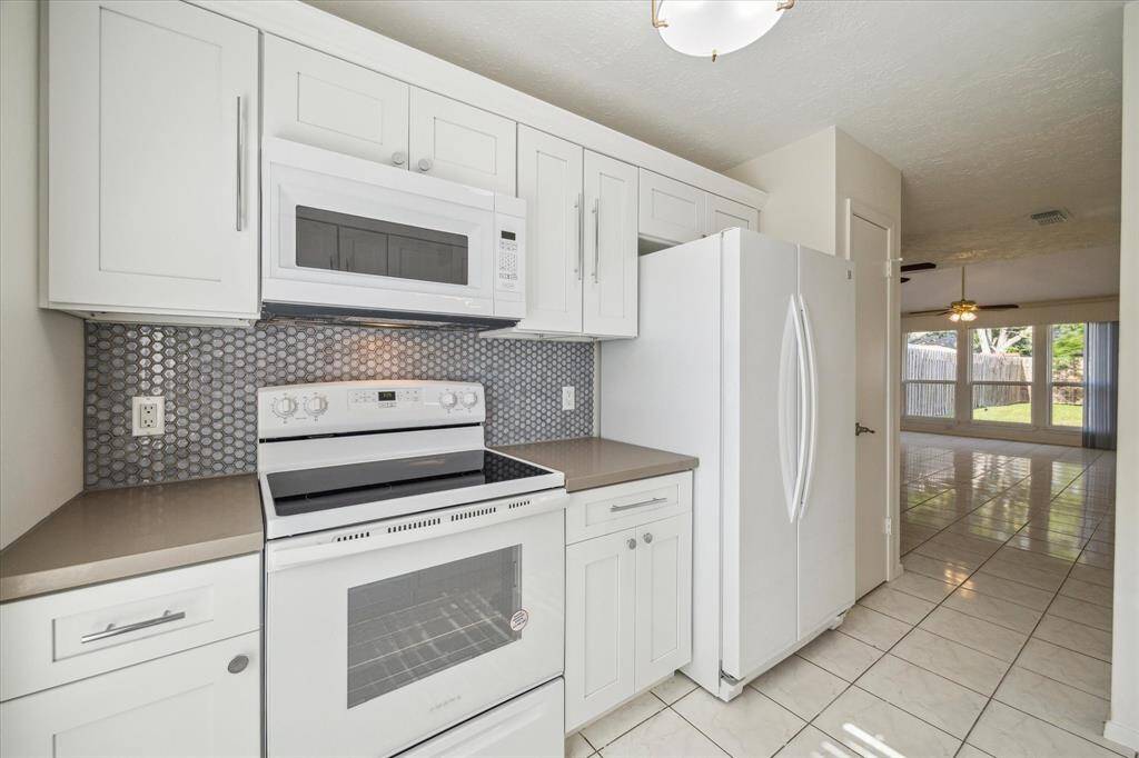 Modern kitchen electric range, built-in microwave, and stylish tile backsplash. Fresh white cabinetry and tile flooring throughout.