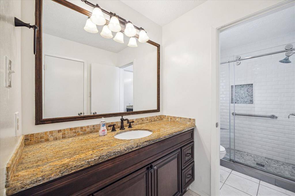 Updated primary bathroom with granite vanity, framed mirror, oil-rubbed bronze fixtures, and a walk-in shower with subway tile and glass doors.