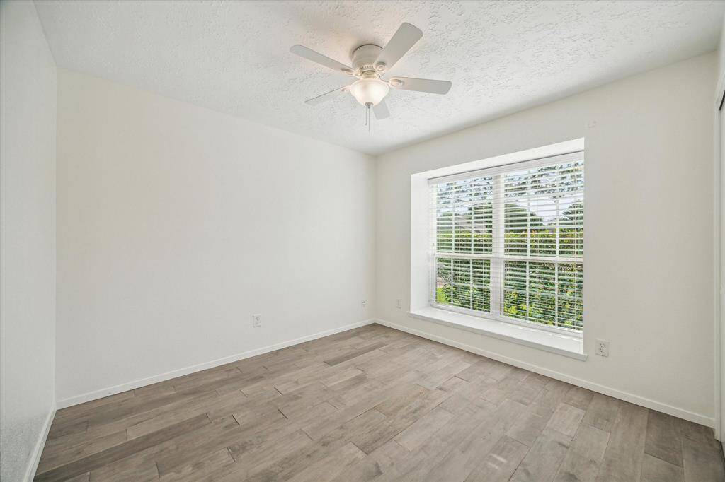 Bright secondary bedroom featuring stylish wood-look tile, a spacious bay window, and a ceiling fan for added comfort.
