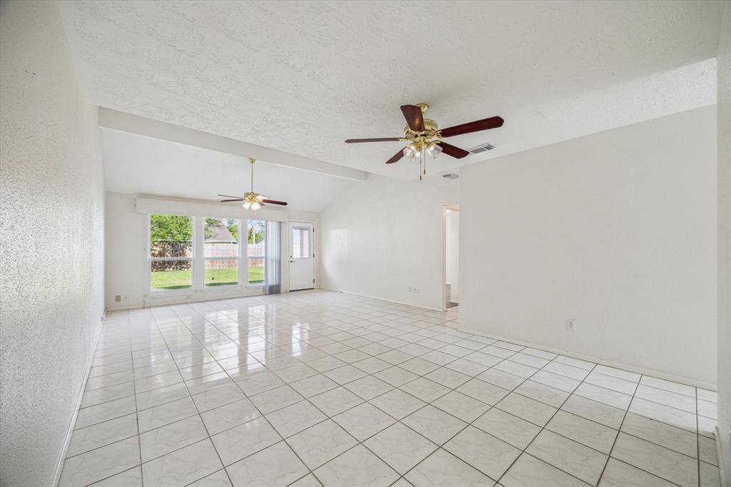 Bright and spacious living area with large windows, tile flooring, and ceiling fans. It offers plenty of natural light and a view of the backyard.