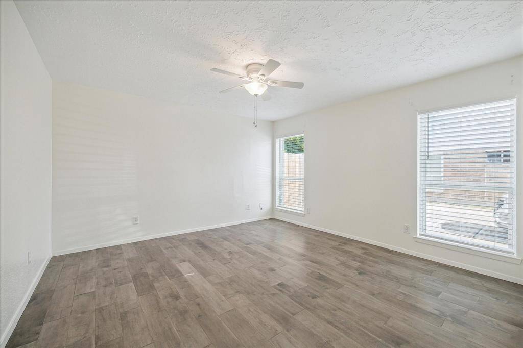 Spacious primary bedroom with wood-look tile flooring, large windows for natural light, ceiling fan, and a walk-in closet.