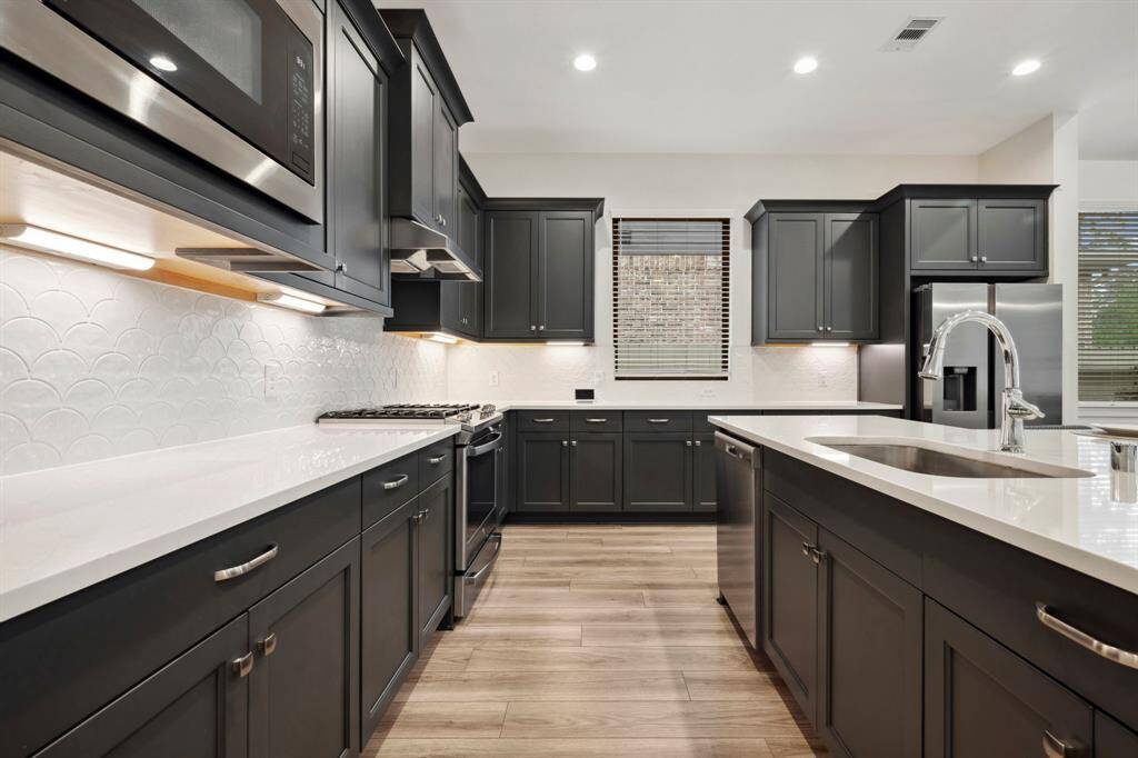 This modern kitchen features sleek dark cabinetry, stainless steel appliances, and a stylish tile backsplash. It boasts a spacious layout with a large island and ample counter space, perfect for cooking and entertaining.
