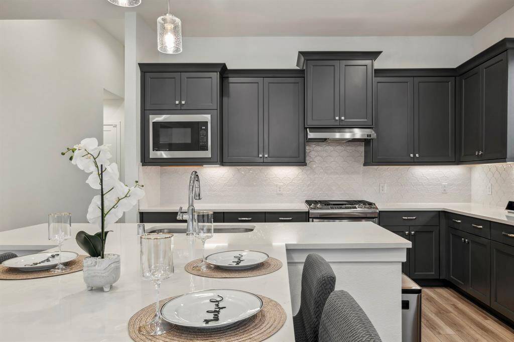 This modern kitchen features sleek, dark cabinetry, a built-in microwave, and a stylish backsplash. The spacious island offers seating and a contemporary feel, complemented by pendant lighting and elegant decor.