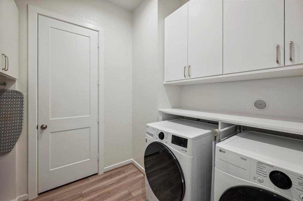 This is a modern laundry room featuring a washer and dryer set under sleek white cabinets for ample storage. The room has a clean, bright appearance with light-colored walls and flooring, offering a functional and organized space.