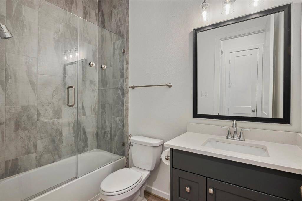 This modern bathroom features a sleek design with a glass-enclosed shower, gray tiled walls, and a dark vanity with a large mirror. The space is well-lit with stylish light fixtures, offering a clean and contemporary look.