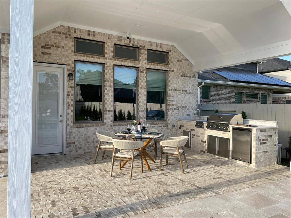This outdoor space features a covered patio with a modern dining area and built-in grill station, perfect for entertaining. The brick exterior and large windows enhance the inviting atmosphere.