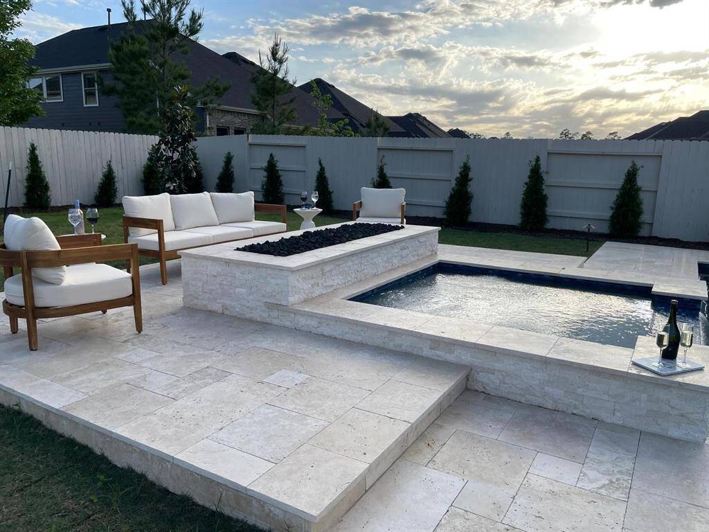This outdoor space features a modern patio with elegant stone tiles, a small pool, and a fire pit. Comfortable seating and a privacy fence create a relaxing atmosphere, ideal for entertaining or unwinding.