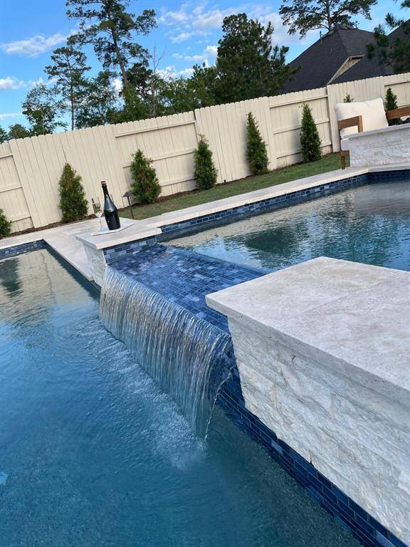 This photo showcases a luxurious backyard with a spacious swimming pool surrounded by a tiled patio. Comfortable wooden lounge chairs with plush cushions are positioned poolside, perfect for relaxation. The area is framed by a well-maintained lawn and privacy fence, offering a serene outdoor retreat.