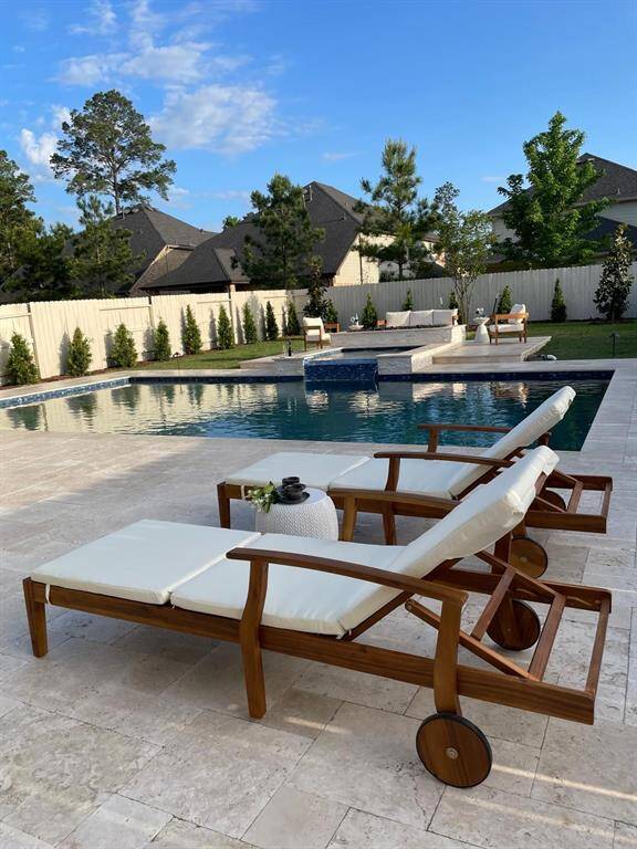 This photo showcases a luxurious backyard featuring a spacious pool with a waterfall feature, surrounded by a landscaped garden. The pool area includes elegant wooden lounge chairs with white cushions, perfect for relaxation. The setting is private and serene, ideal for outdoor enjoyment.