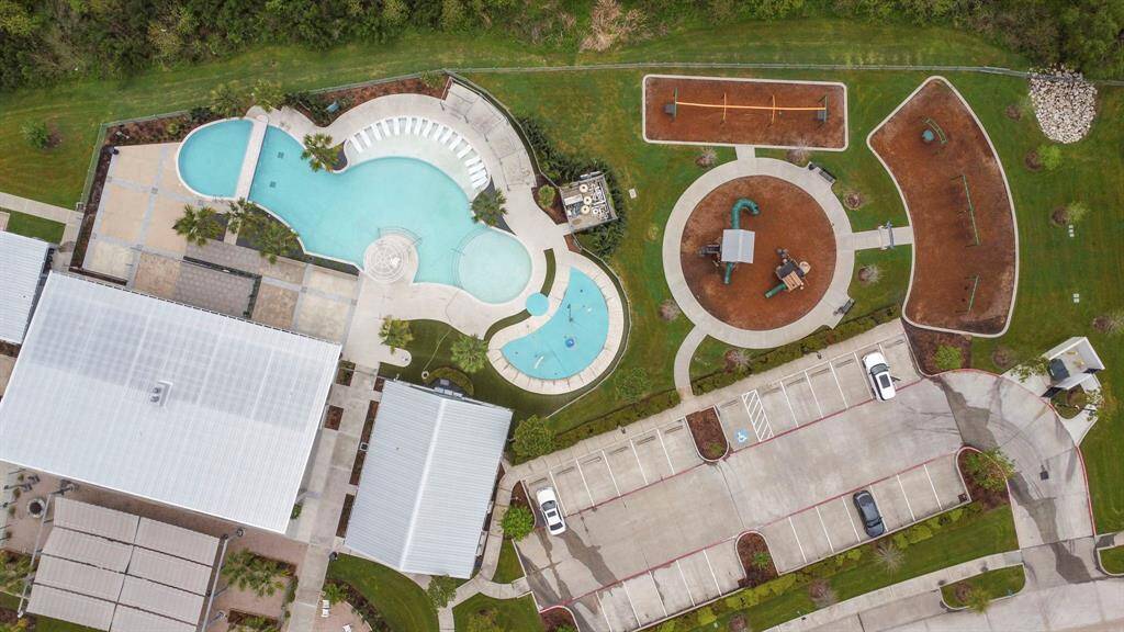 This aerial view showcases a community area with a large pool, a spacious playground, and ample parking. The grounds are well-maintained with green spaces and pathways, ideal for families and outdoor activities.