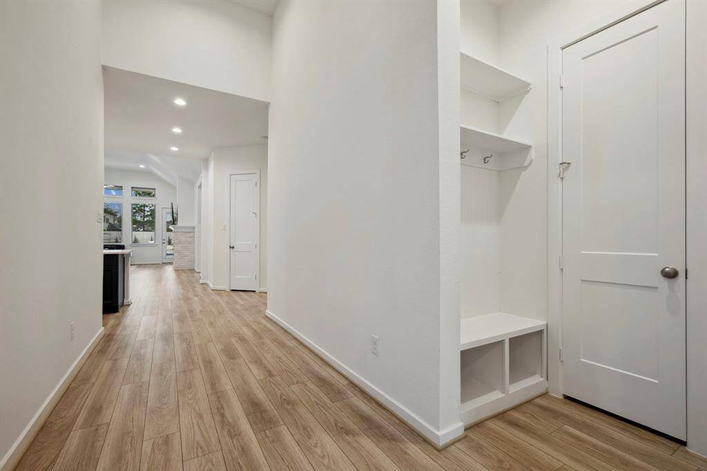 Bright and spacious hallway with light wood flooring, leading to an open living area. Features built-in storage and a modern, clean design with recessed lighting.
