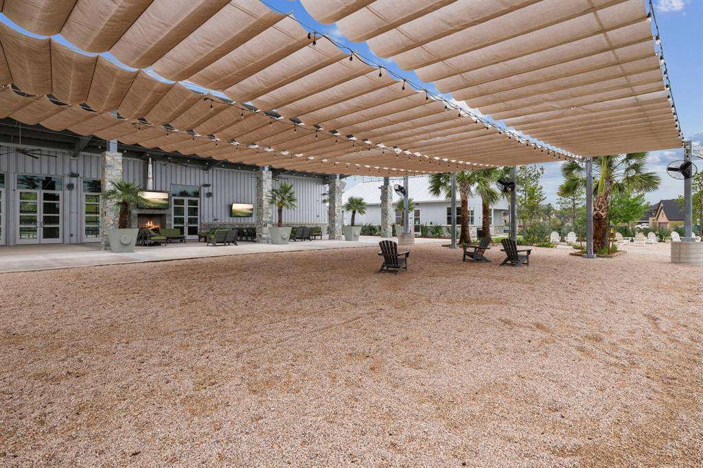 Spacious outdoor area with a modern pergola providing shade over a gravel surface. Features include cozy seating, a fireplace, and surrounding greenery, perfect for relaxation or entertaining.