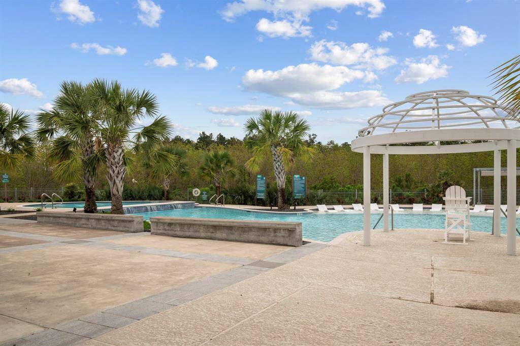 This photo showcases a spacious, inviting pool area with palm trees, a pergola, and ample lounge seating, perfect for relaxation and entertaining.