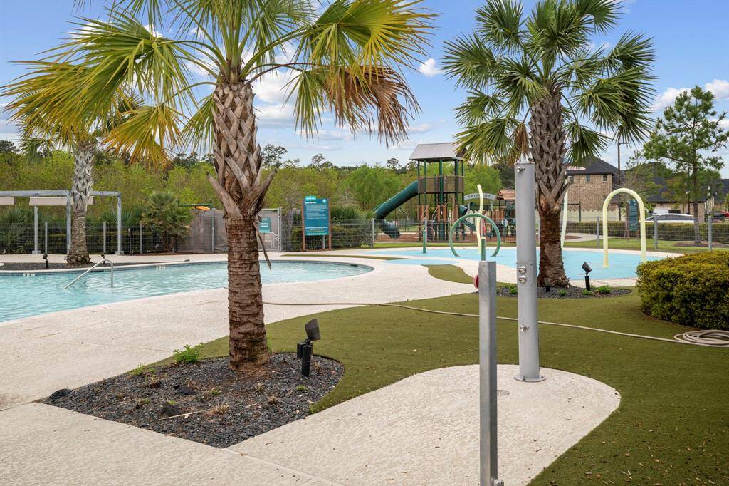 This photo showcases a community pool area with palm trees, a children's playground, and a splash pad, offering a relaxing and family-friendly environment.