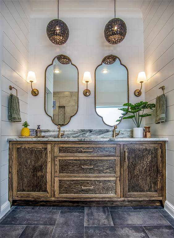 Stunning custom cabinetry, tile wall behind mirrors, designer lighting, mirrors, & trim. Luxurious leathered granite counters with raised shelf behind the undermount sinks.