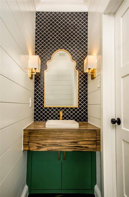 Spectacular half bathroom on the main floor features custom-built wood vanity, tile backsplash extending to the ceiling, soft lighting, wood shiplap walls, & gorgeous trim.