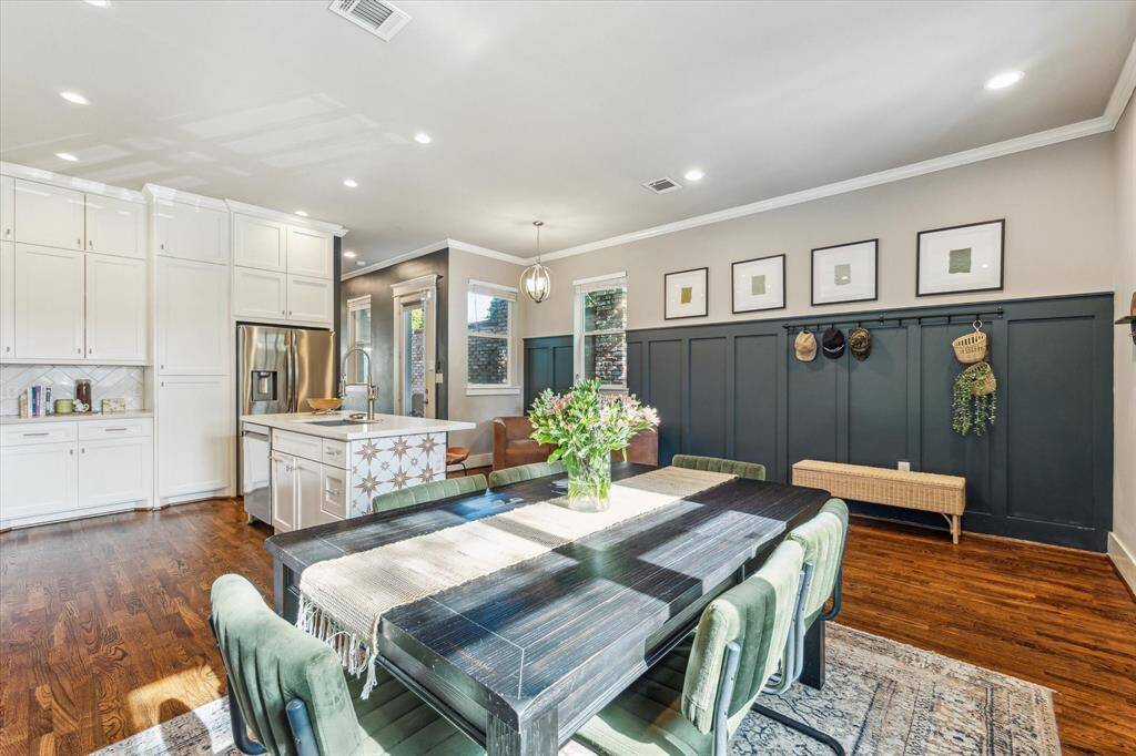 Welcome to 1004 Enid Street B. A charming multi-story house with a light blue facade and brick accents. It features a welcoming wooden door, large windows, and a small balcony. The property is framed by mature trees, providing shade and adding to its curb appeal.