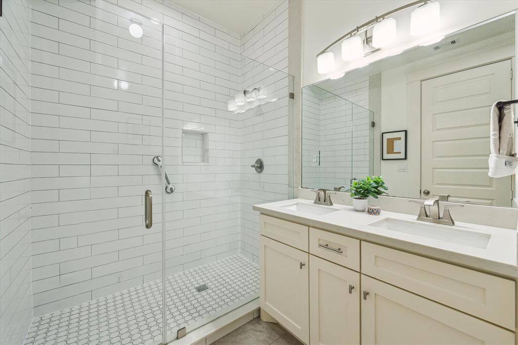 This bathroom features a modern design with a spacious glass-enclosed shower, white subway tiles, and a dual sink vanity with ample storage. The neutral color palette creates a clean and inviting atmosphere.