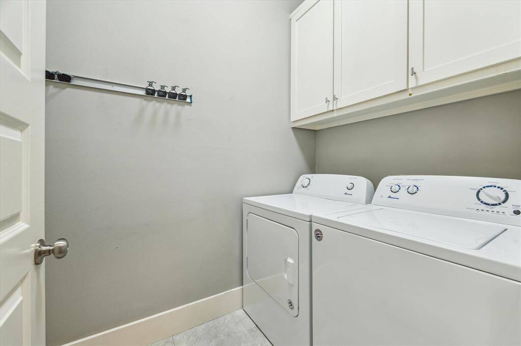 This spacious laundry room is conveniently located on the second floor and comes with a washer and dryer set. There are cabinets above for storage and a wall-mounted rack for hanging items.
