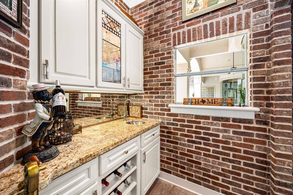 The wet bar features brick accent walls, built-in cabinetry, a prep sink, and a window that opens to the outdoor pool area
