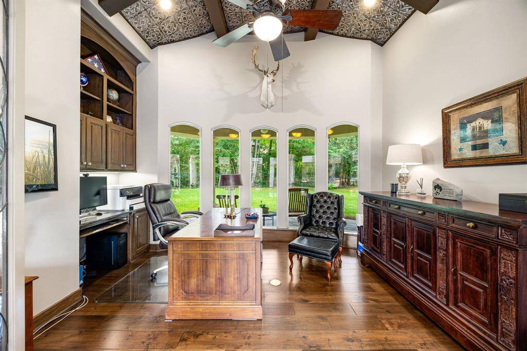 The home office features soaring ceilings accented with rich wood beams, creating a warm yet professional atmosphere ideal for focused work or quiet study.