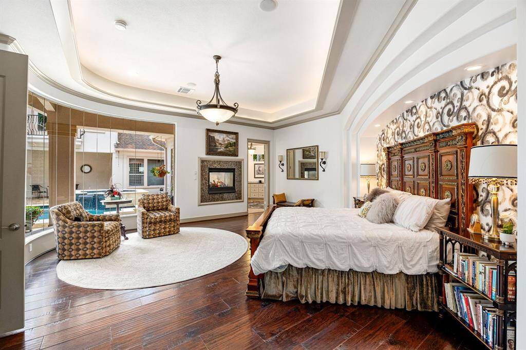 The spacious primary suite features elegant, curved windows, a cozy fireplace, and a relaxing sitting area — all beneath a beautiful tray ceiling.