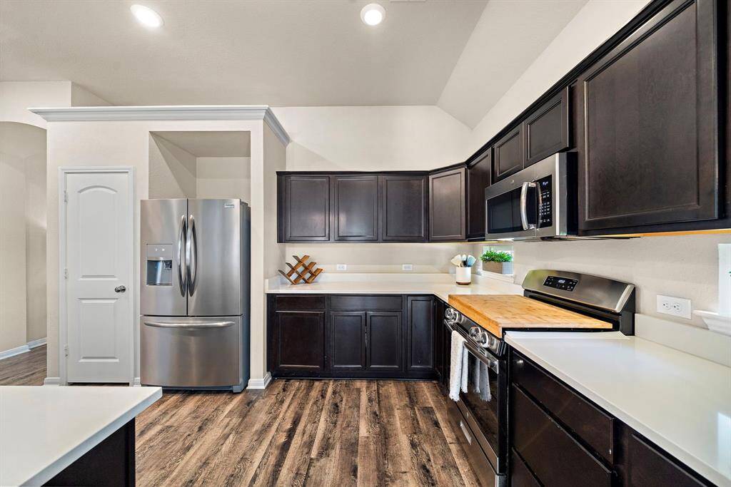 Rich espresso cabinetry and sleek quartz countertops define this kitchen, which offers abundant prep space and a full suite of stainless steel appliances, including a gas range and built-in microwave. Modern touches like a butcher block insert, ample pantry storage, and a large French door refrigerator cater to both convenience and culinary inspiration.