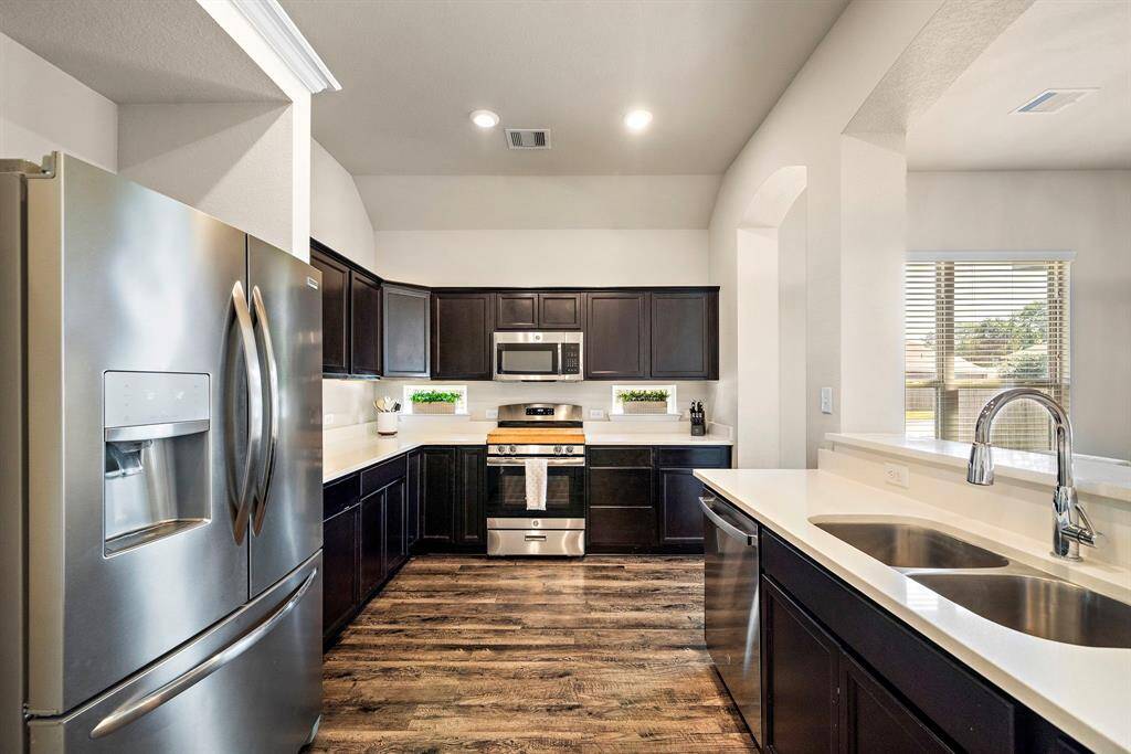 Expansive U-shaped kitchen features sleek stainless steel appliances, a spacious dual sink, and modern quartz countertops. Ample dark cabinetry provides abundant storage, while the open breakfast bar and contemporary backsplash bring extra convenience to this well-designed space.