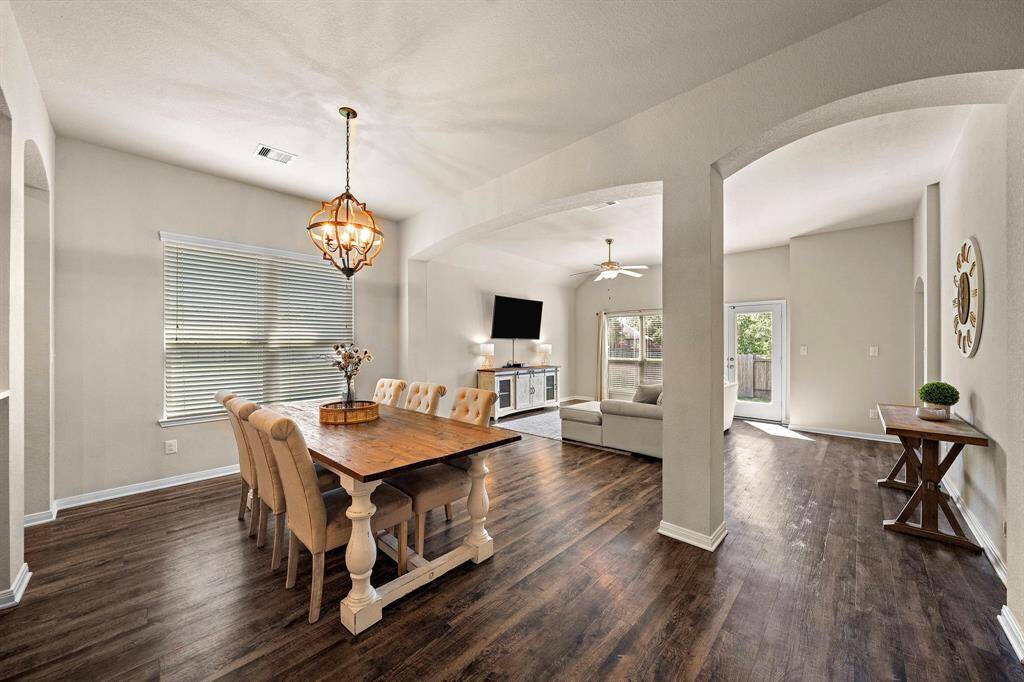 Step into a spacious formal dining area comfortably accommodating a large table for 4-8, highlighted by an elegant statement chandelier and wood-look flooring. The open-concept layout seamlessly connects the dining space to the living area, creating an inviting flow ideally suited for gatherings and entertaining.