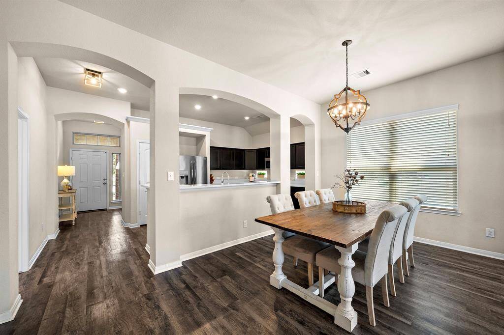 Formal dining area boasts an oversized window for abundant natural light and features a statement orb chandelier centered above a rustic wood table. Elegant arched openings frame the space, providing seamless flow to both the kitchen and foyer for easy entertaining.