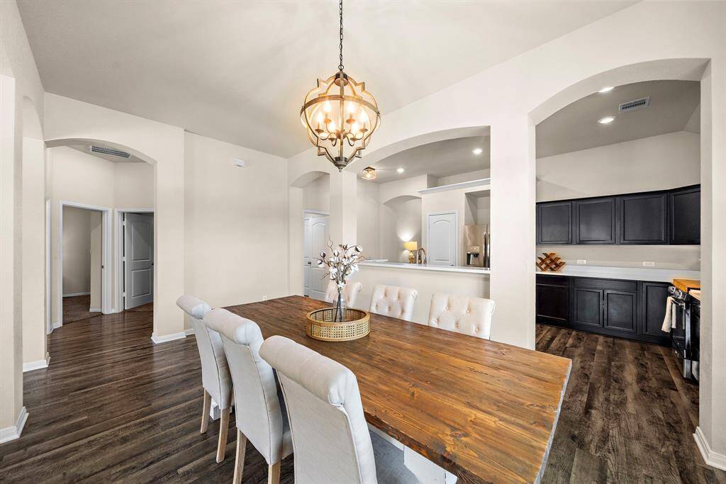 Spacious formal dining room features a striking wood table for 4-8, elegant upholstered seating, and a statement chandelier overhead. Three graceful arched openings create seamless sightlines to the kitchen and adjoining rooms, while rich wood-look floors add warmth and sophistication for gathering and entertaining.