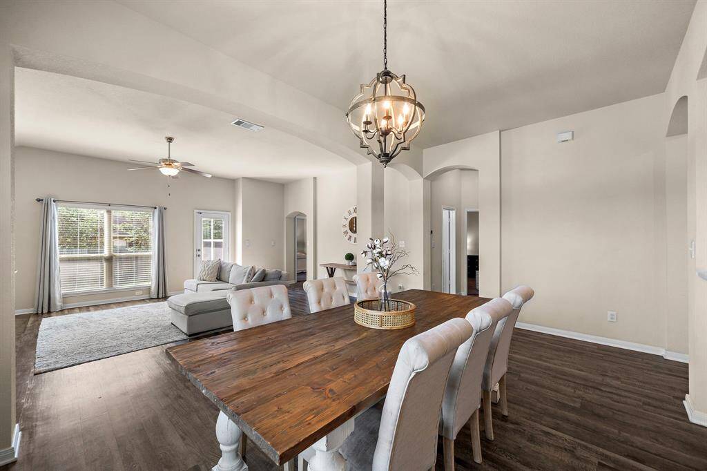 Elegant dining area seamlessly connects to the expansive living room, offering an effortless flow for entertaining or daily life. Architectural arches, a rustic wood table for 4-8, and an eye-catching pendant light lend sophistication, while rich wood-look floors and generous natural light enhance the atmosphere.