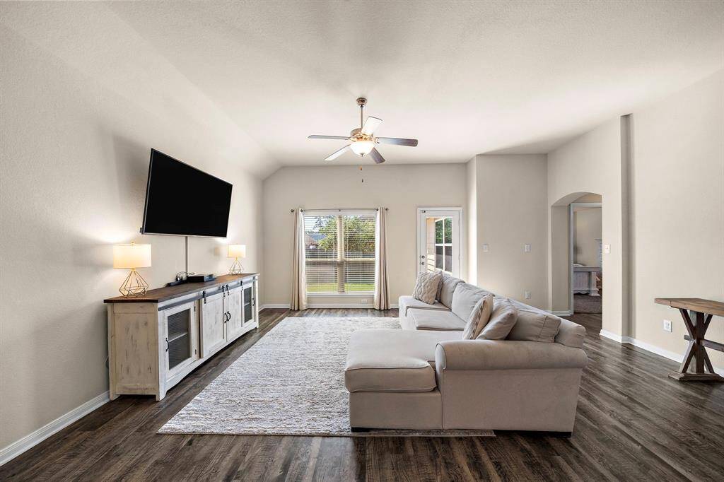 Spacious living room boasts vaulted ceilings, rich wood-look floors, and a generous seating area ideal for relaxing or entertaining. Natural light pours in through the large windows and patio door, while a convenient study nook and seamless flow to adjacent rooms highlight the home’s open-concept design.