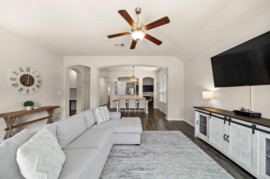 Spacious living area showcases a large sectional and built-in media console, creating an inviting setting for relaxation or movie nights. Open sightlines to the dining space, wood-look floors, and triple arched doorways highlight the seamless flow and generous scale of the home’s layout.