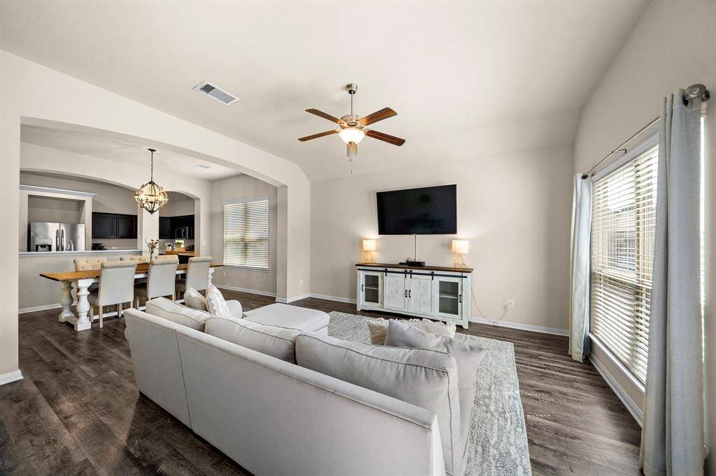 Expansive living area seamlessly connects to the gourmet kitchen and formal dining, creating an open flow ideal for gatherings or relaxing evenings. Vaulted ceilings and large windows fill the space with natural light, while a crisp palette and wood-look floors offer warm modern elegance.